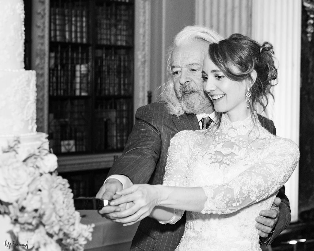 Black and white image of couple cutting luxury wedding cake By Yevnig