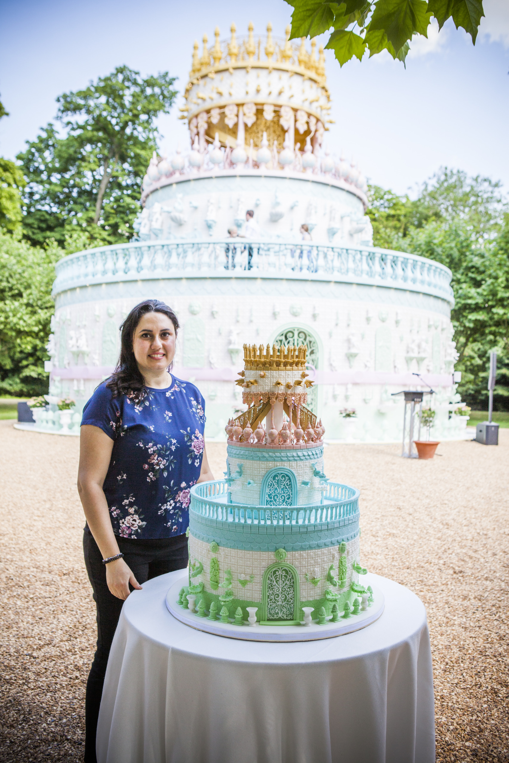 Yevnig Davis Creative Director of By Yevnig, stands next to her creation The Wedding Cake By Yevnig which sits in front of the Wedding Cake Folly, by Joana Vasconcelos at Waddesdon Manor