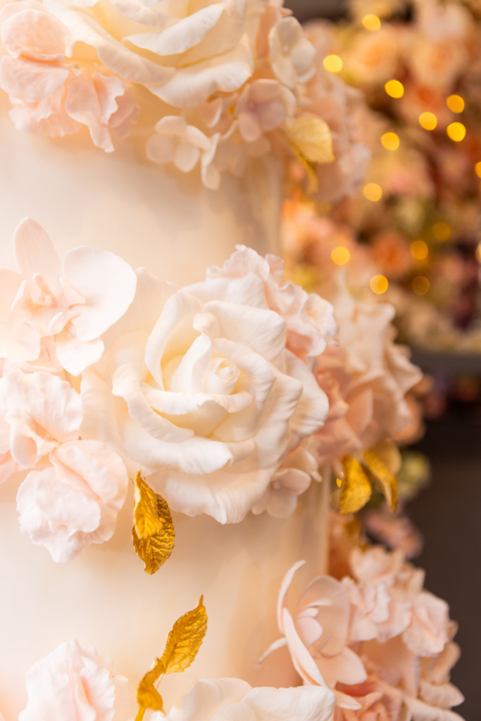 Details of hand-crafted sugar roses on a luxury By Yevnig floral wedding cake in apricot, ivory and blush pink with gold leaves in the window of Neill Strain Floral Couture, Mayfair London.