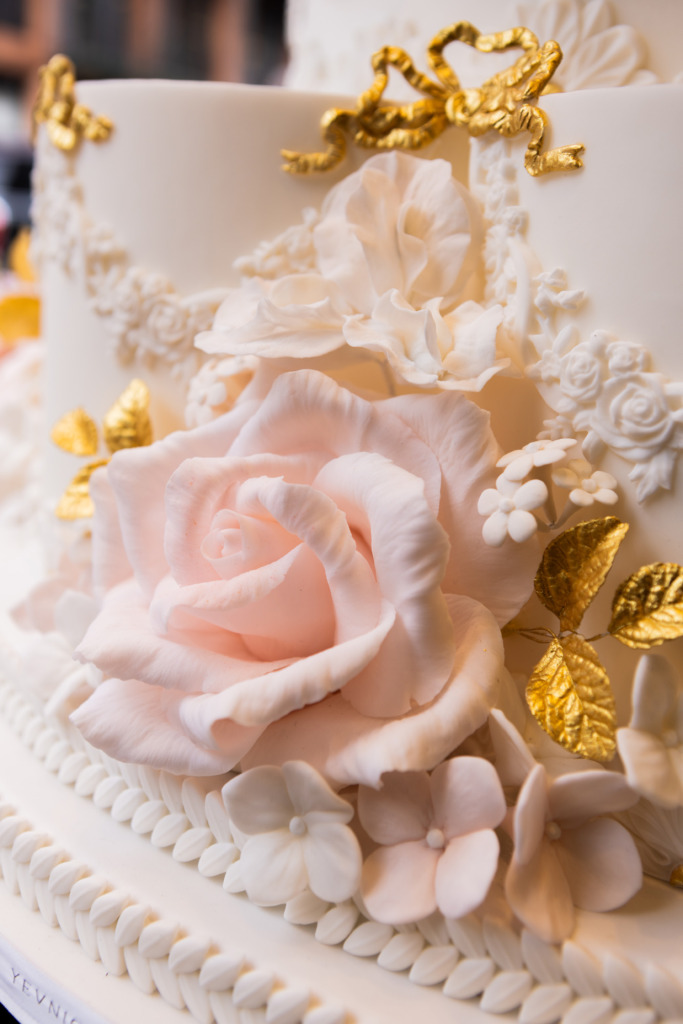 Details of hand-crafted sugar roses on a luxury By Yevnig floral wedding cake in apricot, ivory and blush pink with gold leaves in the window of Neill Strain Floral Couture, Mayfair London.