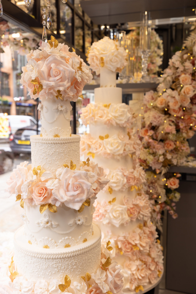 Two luxury floral wedding cakes By Yevnig positioned in the window of Neill Strain Floral Couture, Mayfair, London with fresh floral installation.