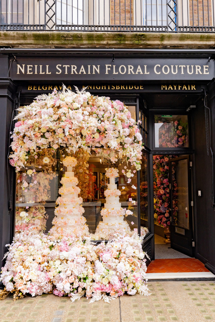 By Yevnig statement floral wedding cakes in the window of Neill Strain Floral Couture, Mayfair London, surrounded by fresh floral installation.